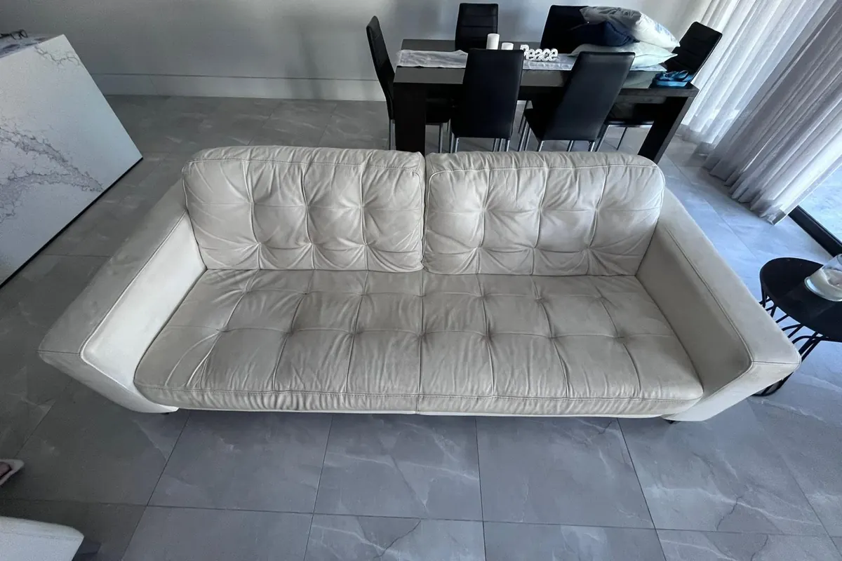 A pale tufted leather sofa after cleaning and conditioning, on a grey tiled floor